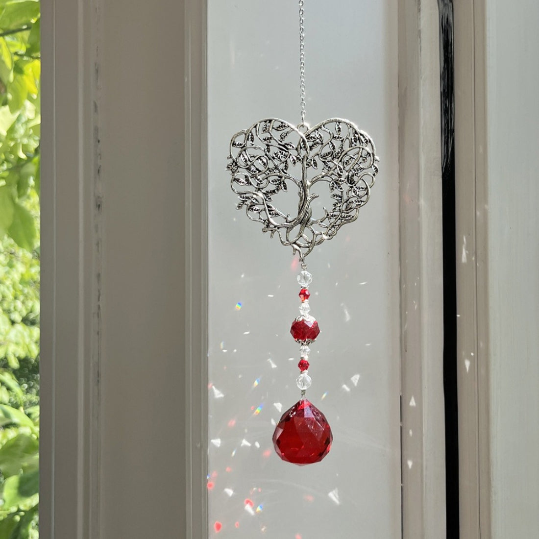 Somnira Heart Tree suncatcher hanging in a window with sunlight shining through beads