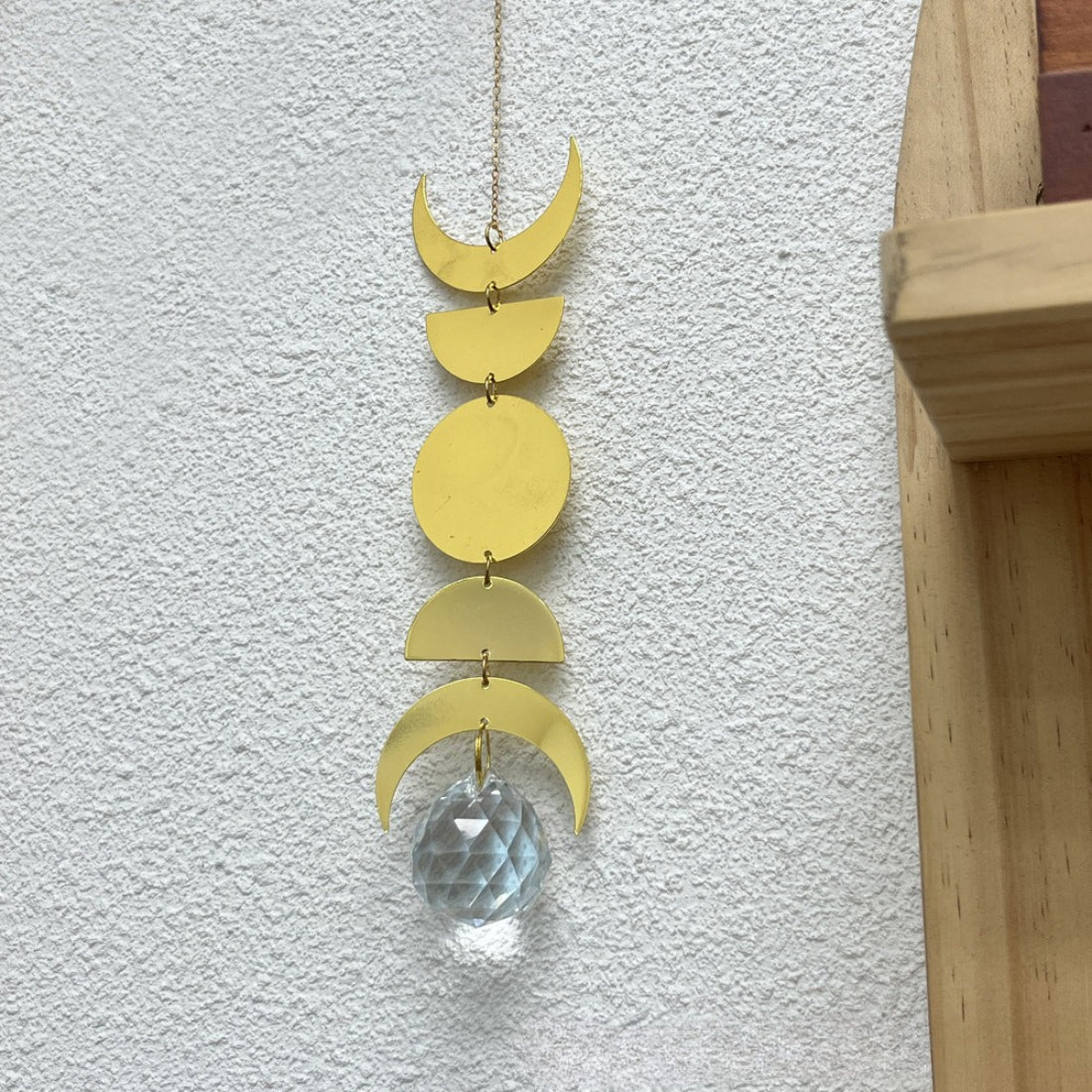 Somnira Moon Phase suncatcher hanging in window with sunlight shining through