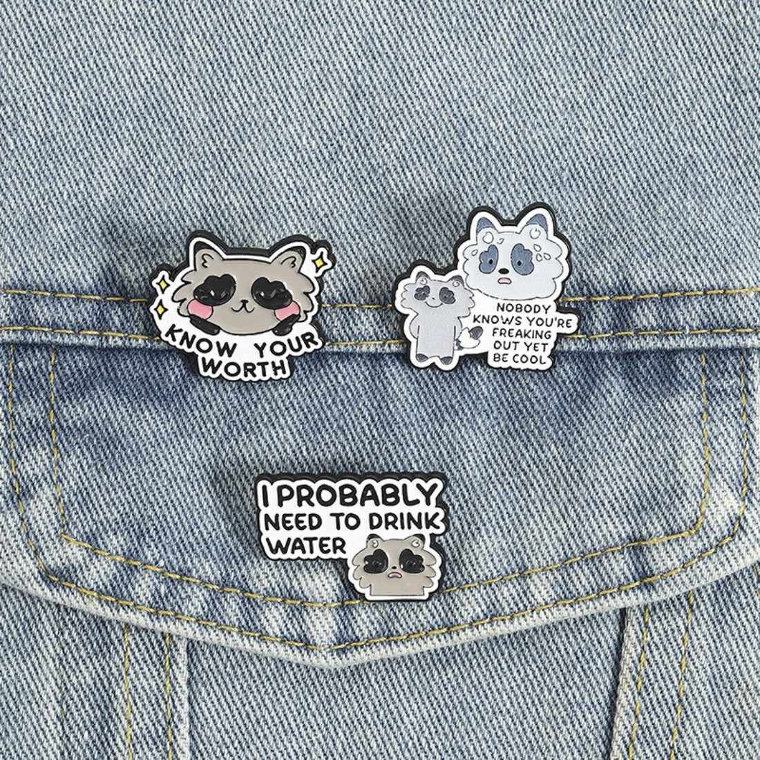 Pinori Positive Raccoon Quote enamel pin displayed with other colorful enamel pins