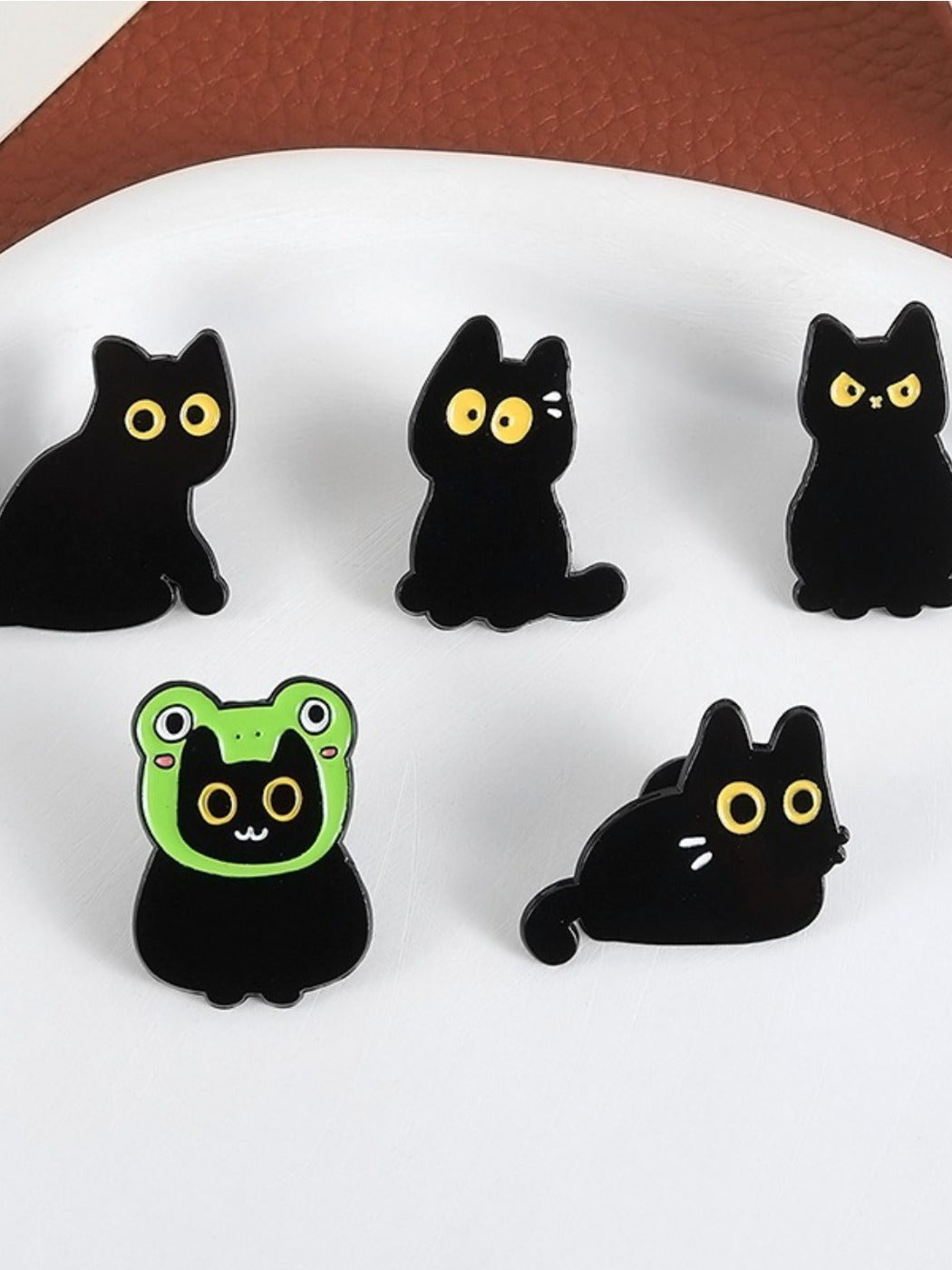 Close-up of Pinori black cat pin with yellow eyes and smiling frog design