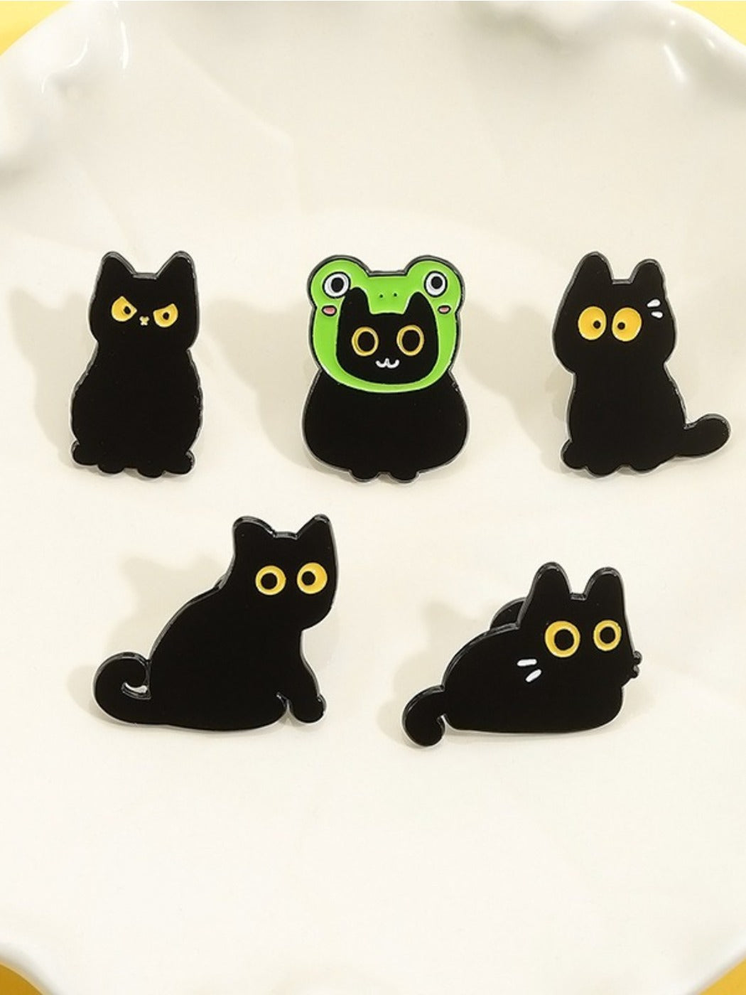 Pinori frog and black cat enamel pin displayed on a fabric surface
