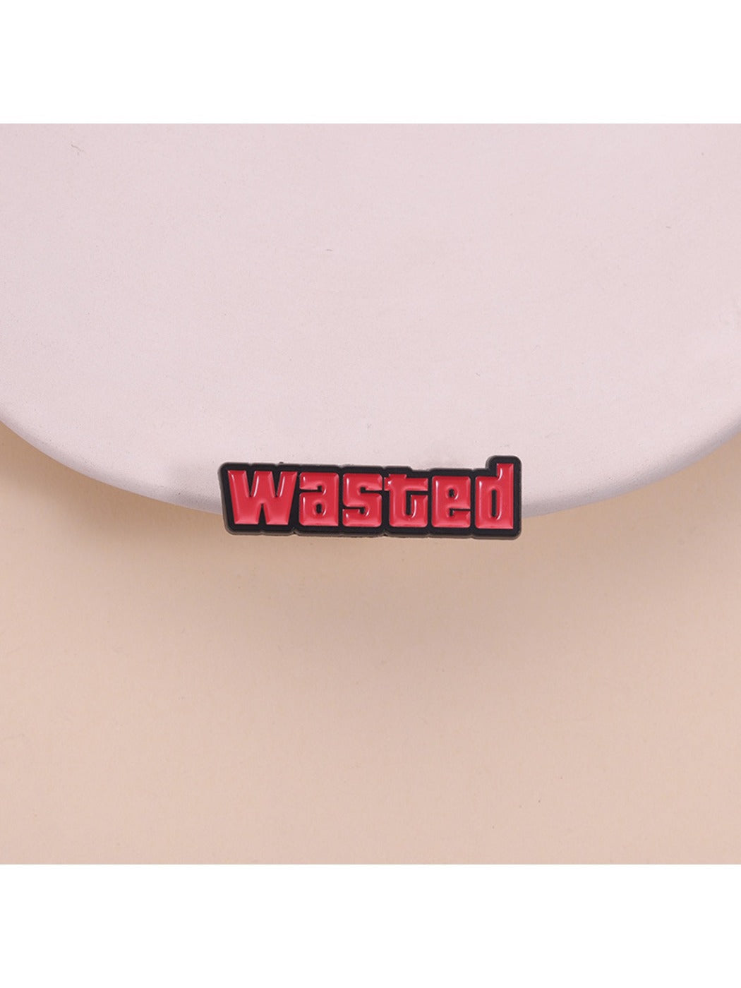 Close-up of Pinori 'Wasted' text pin with black and white design on a white background