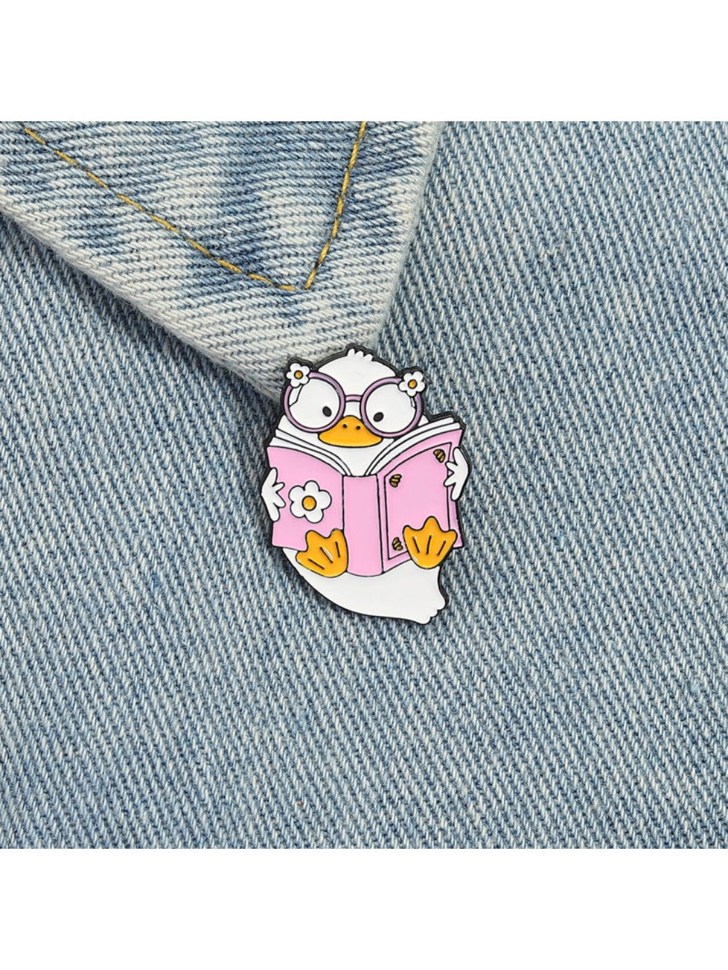 Close-up of Pinori pink reading book brooch with a small duck figure on a plain surface