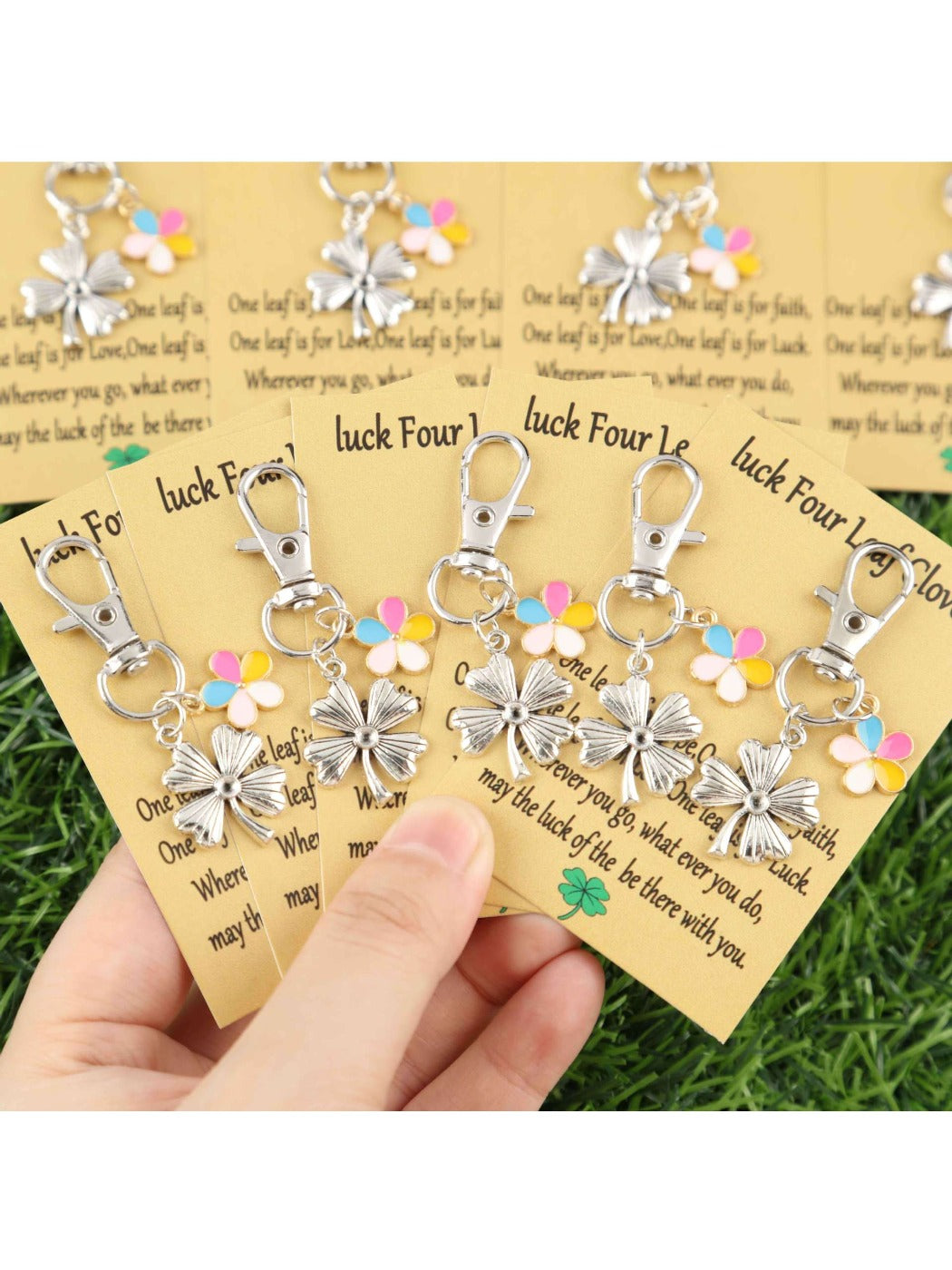 Hand holding several colorful lucky clover and flower keychains against a plain background
