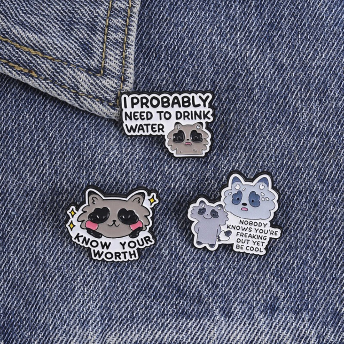 Pinori Positive Raccoon Quote enamel pin held between fingers showing size and detail
