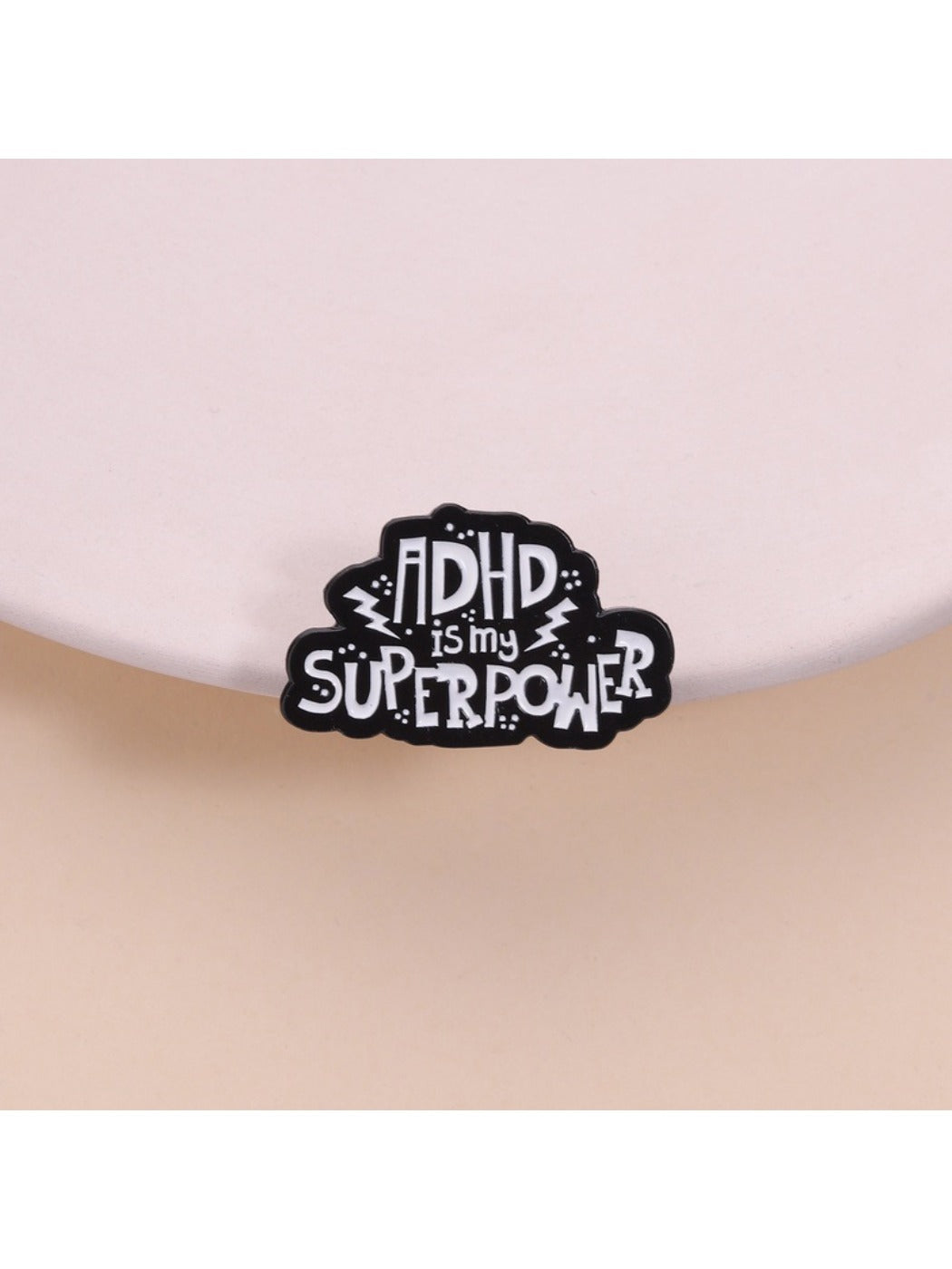 Close-up of Pinori pin badge with 'ADHD Is My Superpower' text on white background